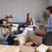 Friends sitting and talking in their new apartment while unpacking their things from cardboard box.